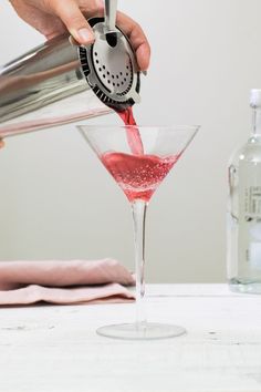 a person pours red liquid into a martini glass with a strainer in it