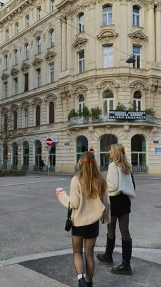 two women walking down the street in front of a large building with lots of windows