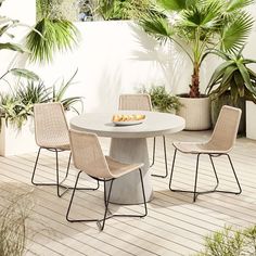 a white table with four chairs around it on a wooden floor next to potted plants