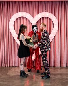 three people standing in front of a heart - shaped backdrop with flowers and makeup on