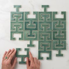 someone is making a puzzle out of green tiles on the wall with their hands and fingers