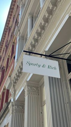 a white sign hanging from the side of a tall building next to columns and windows