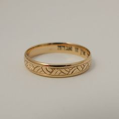 a gold wedding ring with an engraved design on the outside and inside, sitting on a white surface