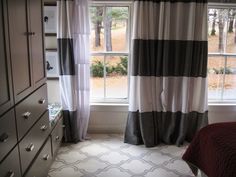 a bedroom scene with focus on the bed and dressers, window curtained in black and white striped drapes