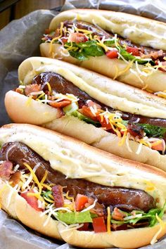 three hot dogs in buns topped with cheese and toppings on tin foil lined up