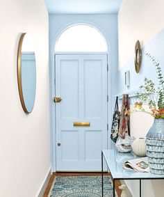 a blue door in a white hallway with an oval mirror and vase on the table