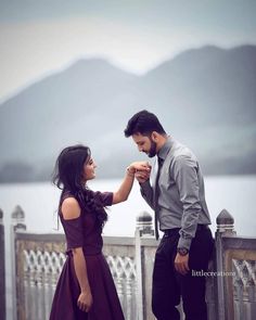 a man and woman standing next to each other on a bridge with mountains in the background