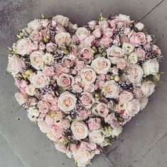 a heart - shaped arrangement of pink and white flowers on the ground with grey cement