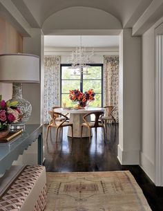 a dining room with a table and chairs next to a vase filled with flowers on top of a rug