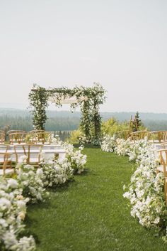 an outdoor ceremony set up with white flowers and greenery on the grass, surrounded by wooden chairs