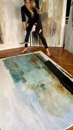 a woman is painting on the floor in front of a large piece of art that has been painted