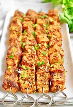 several skewers are lined up on a white plate with green garnishes