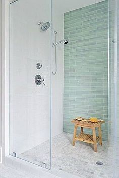 a walk in shower sitting next to a wooden stool on top of a white tiled floor