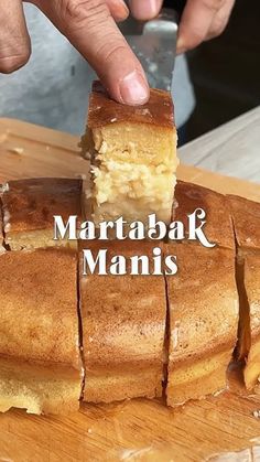 a person is cutting into a cake on a wooden board with the words marbatak manis above it