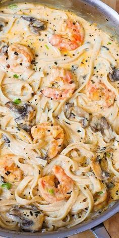 a pan filled with pasta and shrimp on top of a wooden table next to a purple frame