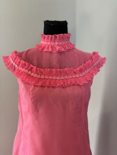 What a find! Classic 60's Lori Deb san Fransisco label. Sheer hot pink material floats over a lining of the same color. The high neck and sheer bodice above the bust features accordion pleated lace accented with a daisy trim. There are darts and princess seams on the bodice. The sheer outer layer is slightly gathered in the back, falling gracefully from the shoulder seam. The dress closes with a hidden nylon zipper. The dress is in very good vintage conditions. There is some damage to the lining High Neck Pink Top For Summer, Pink High Neck Top For Summer, Pink Ruffled Top For Evening, Pink Sleeveless Evening Blouse, Pink Ruffled Tops For Wedding, Fitted Retro Pink Blouse, High Neck Summer Party Blouse, High Neck Summer Blouse For Party, Pink Ruffled Tops For Formal Occasions