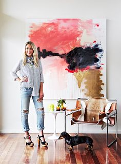 a woman standing in front of a painting with a dog on the floor next to her