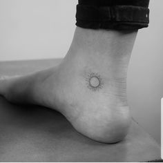 a black and white photo of a person's foot with a small sun tattoo on it