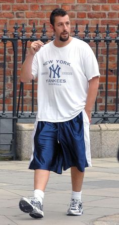 a man is walking down the street with his foot in the air while wearing blue shorts and a new york yankees t - shirt