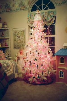 a white christmas tree with pink lights in a room next to a doll house and window