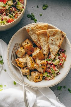 a white plate topped with pita bread next to a bowl of salad and a fork