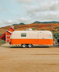 an orange and white trailer parked in front of a red barn