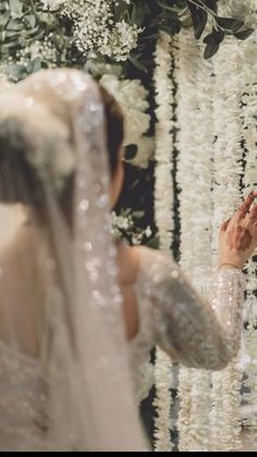 a woman in a wedding dress looking at herself in the mirror with flowers all around her