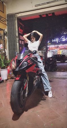 a woman sitting on top of a red motorcycle in front of a building with neon lights