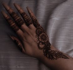 a woman's hand with henna tattoos on her left arm and fingers, resting on a bed sheet