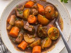 a white bowl filled with stew and carrots on top of a table next to some parsley