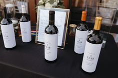 four bottles of wine sitting on top of a table next to a framed photo and flowers