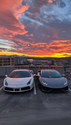 two cars parked next to each other in a parking lot with the sun setting behind them