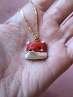 a hand holding a small red and white fox necklace