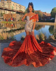 a woman standing in front of a lake wearing a red and silver dress with sequins on it