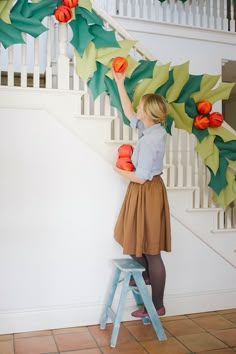 a woman is standing on a step ladder and decorating a christmas wreath with paper flowers