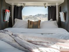 a bed with white sheets and pillows in a room next to a window that looks out onto the mountains