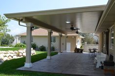 a covered patio with chairs and tables in front of a house on a sunny day