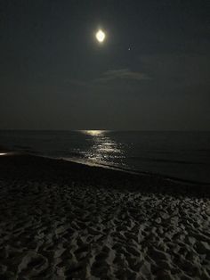 the moon is shining over the ocean on a beach at night with no one in it