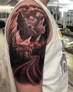 a man's arm with a mountain scene on it and a road going through the mountains