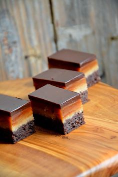 four pieces of chocolate dessert sitting on top of a wooden cutting board