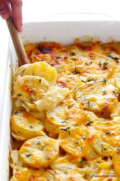 a casserole dish with potatoes and cheese being spooned into the casserole