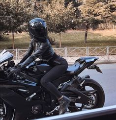 a woman in black riding on the back of a motorcycle