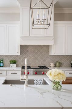 a white kitchen with marble counter tops and an island in front of the stove top