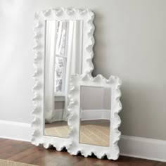 a large white mirror sitting on top of a wooden floor next to a rug and window