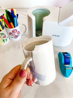 a person holding a cup in front of some crayons and other office supplies