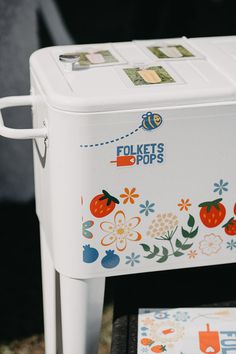 a white cooler sitting on top of a table next to a box with stickers on it