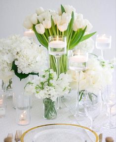 white flowers and candles are arranged on a table with gold rimmed plates, silverware and glasses