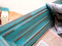 a person is holding an open book in front of a blue hammock that has been painted teal