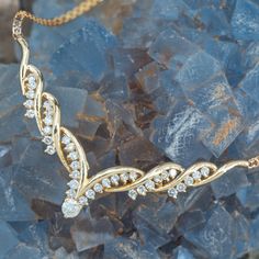 a gold necklace with diamonds on top of some blue rocks and water droplets in the background