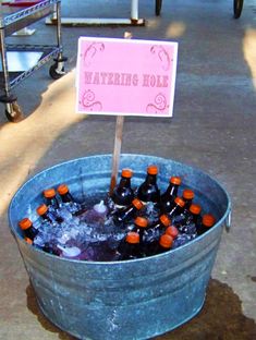 a bucket filled with bottles of beer sitting on top of a sidewalk next to a sign